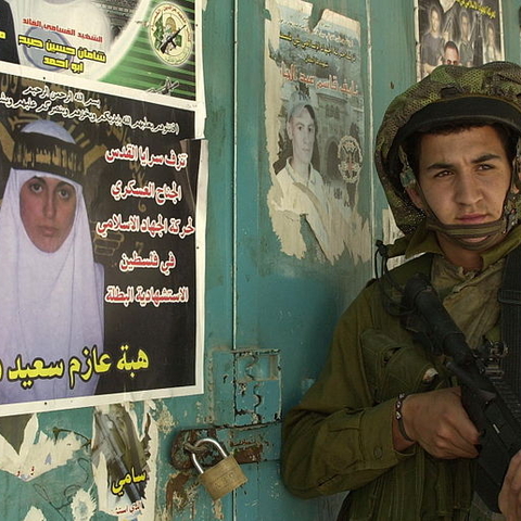 A member of the Israeli Defense Force (IDF) stands next to a poster celebrating an Islamic Jihad operative.