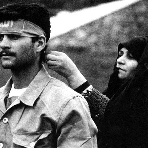 An Iranian woman ties a headband onto a soldier.