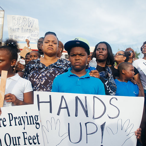 A group of demonstrators stand at a Ferguson, Missouri protest holding signs that read 'Hands Up, Don't Shoot.'