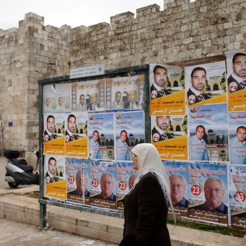 A woman walks by Palestinian Parliamentary Election posters.
