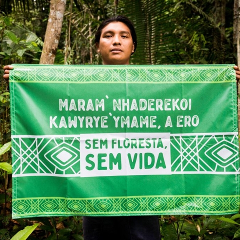 Andre Karipuna holds a banner written in Portuguese and Karipuna.