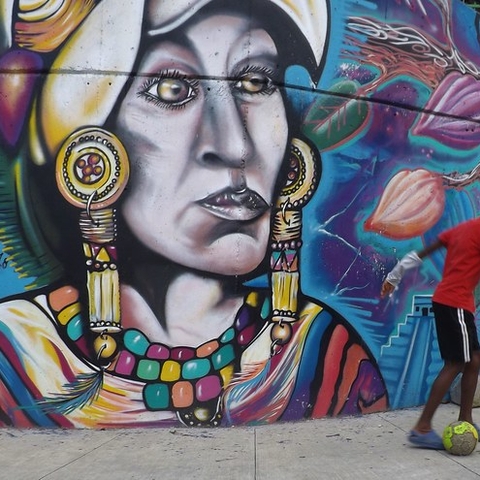 Boys play football in front of a Pachamama mural.
