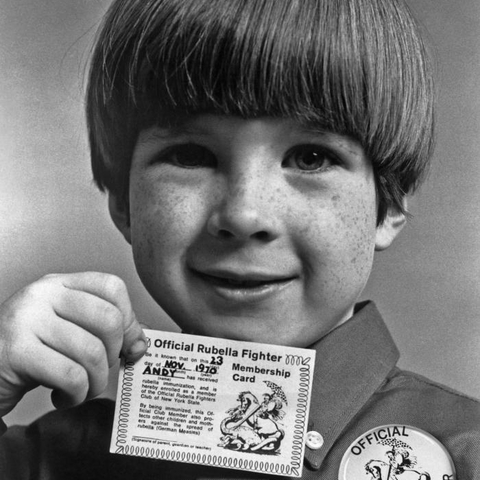 Photograph of a young boy in 1970 showing off his 'Official Rubella Fighter' membership card and button.